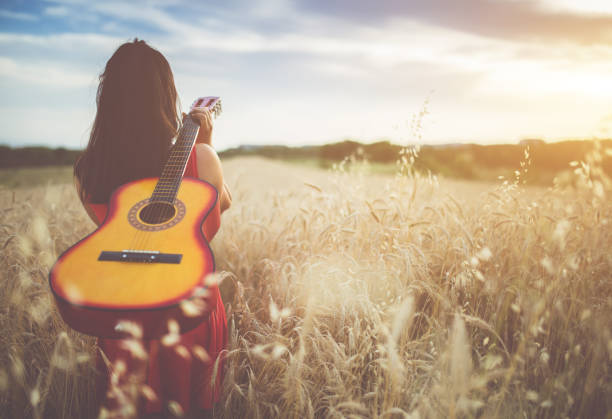 istock Woman walking through the wheat field with guitar on back 1145978052