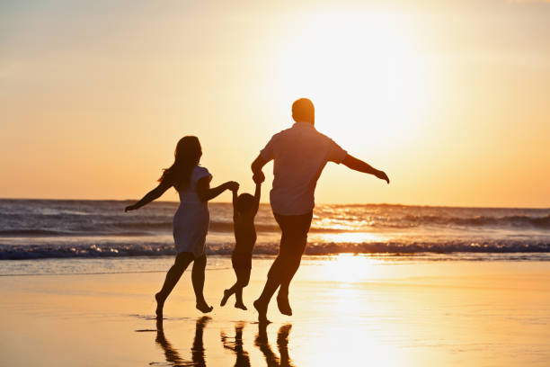 famiglia felice che corre sulla spiaggia al tramonto - women action jumping running foto e immagini stock