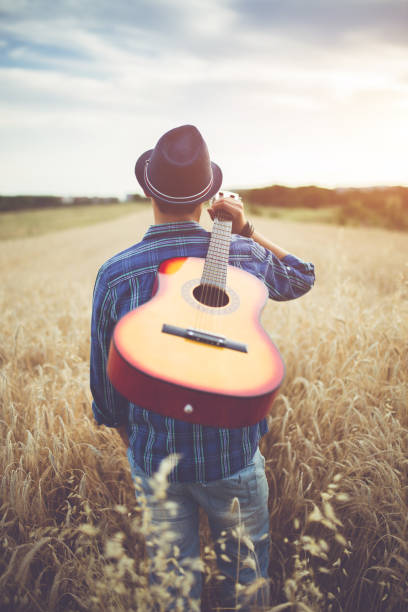 istock Man walking through the wheat field with guitar on back. 1145978682