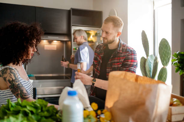 Young man offering his female flatmate a bottle of beer Young man in the kitchen with flatmates offering his female friend a bottle of beer flatmate stock pictures, royalty-free photos & images