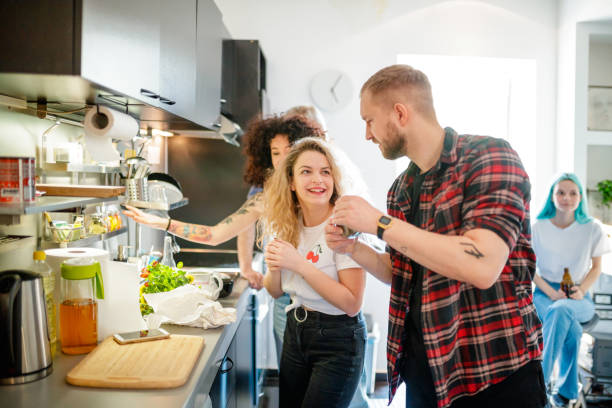 Cheerful young flatmates with friends in the kitchen Cheerful young flatmates with friends in the kitchen preparing food together roommate stock pictures, royalty-free photos & images