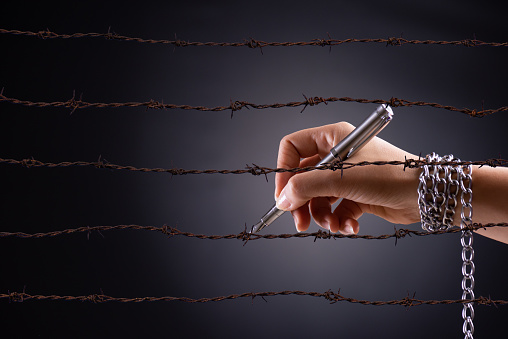 Woman hand with pen tied with chain and rusty sharp bare wire, depicting the idea of freedom of the press or expression. World press freedom and international human rights day concept.