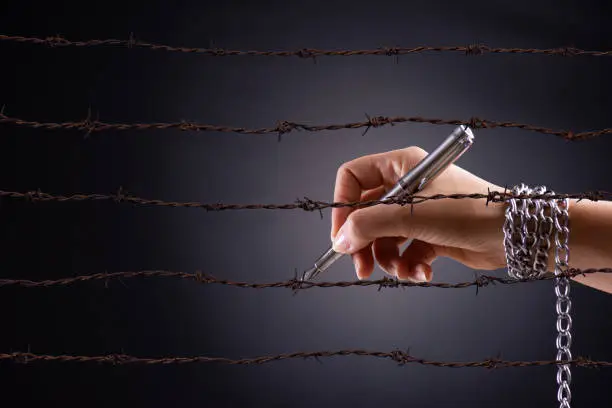 Photo of Woman hand with pen tied with chain and rusty sharp bare wire, depicting the idea of freedom of the press or expression. World press freedom and international human rights day concept.