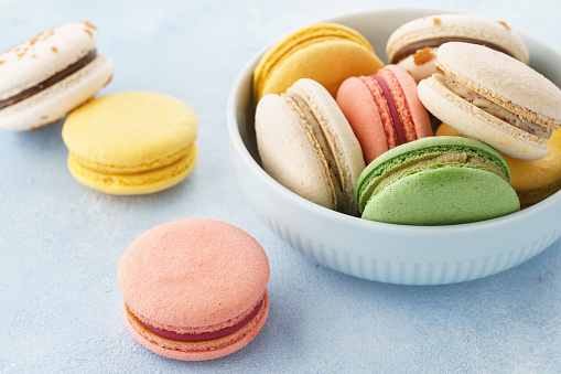 Colorful french macarons with different fillings in a bowl on blue background.