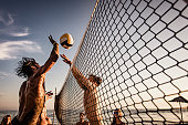 Young man blocking his friend while playing beach volleyball in summer day.