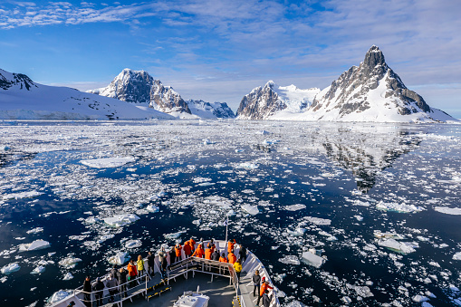 A view of people on a ship bow looking to the northern entrance of the narrow Lemaire channel of the Antarctic Peninsula