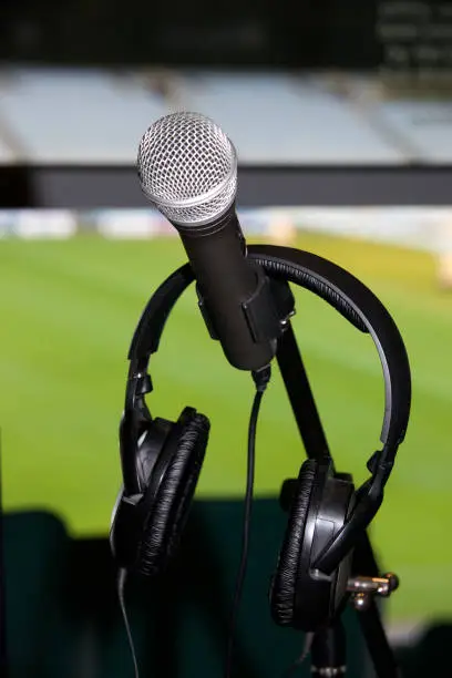 Close-up shot of a microphone and headphones in the sports commentary box of a stadium.