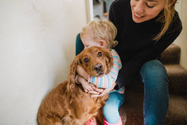 Mother and daughter sitting on the steps of their home ready to go out with their pet cocker spaniel. The young girl is hugging the dog.