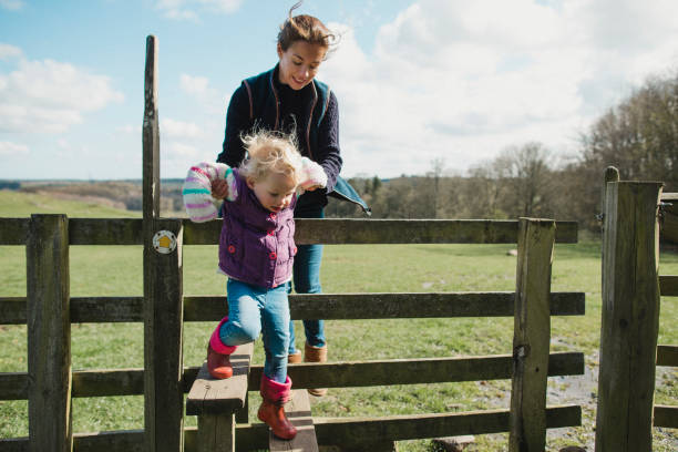 Climbing Over The Stile Mother and daughter out for a walk together. The young girl is climbing over a stile with her mothers help. life stile stock pictures, royalty-free photos & images