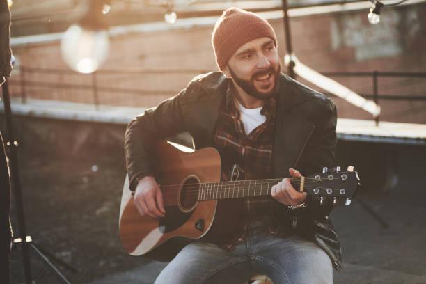 istock Bearded guy in cap playing and singing on the rooftop at nice autumn day 1146005822