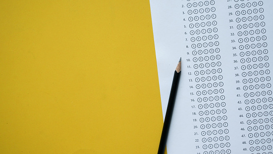 close up top view of black pencil over exam answer sheet paper with multiple choice on yellow background for world literacy day and education concept