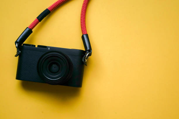 close up top view of black camera with red strap on yellow background for summer travel and fashion accessory concept close up top view of black camera with red strap on yellow background for summer travel and fashion accessory concept strap photos stock pictures, royalty-free photos & images