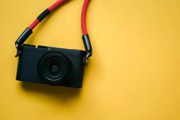 Photo of close up top view of black camera with red strap on yellow background for summer travel and fashion accessory concept
