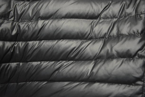 istock Black satin fabric with down filling and gold reflection from a warm female down jacket with lines along the entire fabric. 1146008698