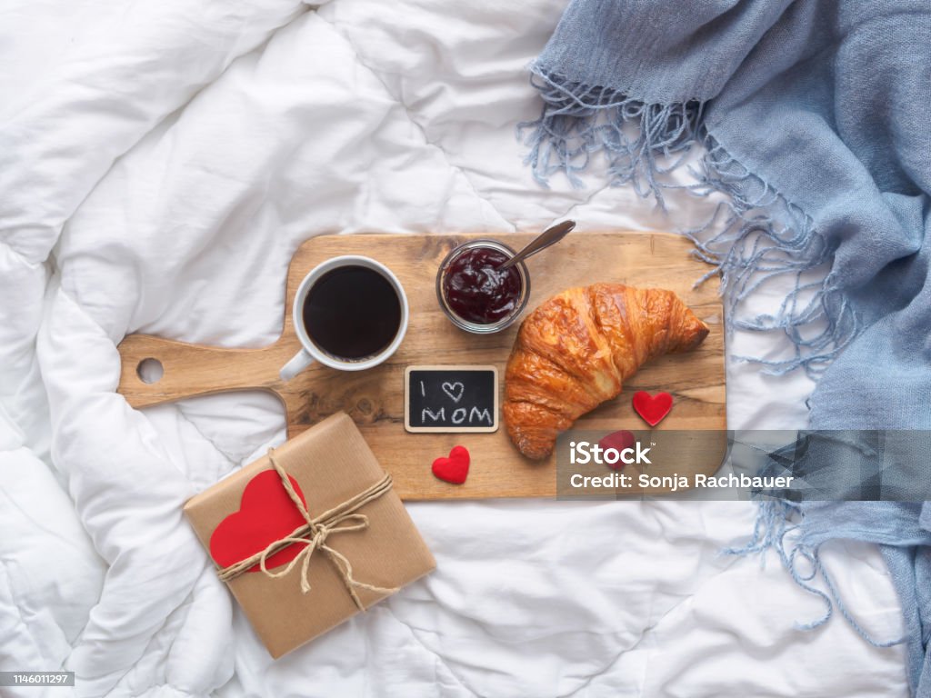 Breakfast in bed, Mother's Day brunch Breakfast with coffee, croissant and jam on a cutting board on a white coverlet, top view, birthday present, paper heart Mother's Day Stock Photo