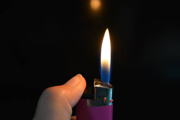 istock On a black glossy background is a woman's hand holding a pink included lighter with a beautiful flame, a bright fire and a reflection. 1146011574