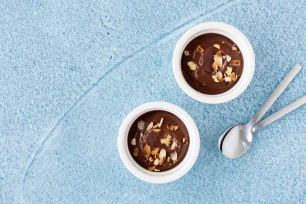 Top view of homemade chocolate dessert in two white ceramic ramekins on blue concrete background with lots of copy space.