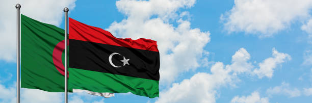 l’algérie et le drapeau de la libye agitent dans le vent contre le ciel bleu nuageux blanc ensemble. concept de diplomatie, relations internationales. - libyan flag photos et images de collection