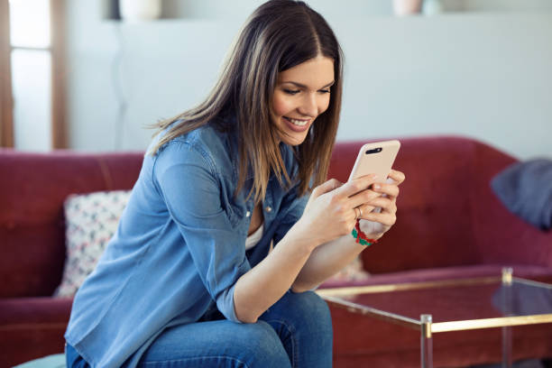 istock Pretty young woman using her mobile phone while sitting on sofa at home. 1146017709