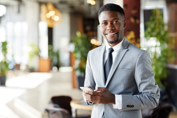 Cheerful young African-American businessman with smartphone Portrait of cheerful confident handsome young African-American businessman with beard using smartphone to text message businessman african descent on the phone business person stock pictures, royalty-free photos & images