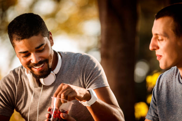 istock Active sportsman taking a handful of berries from his friend's cup while resting from exercising in a city park 1146020061