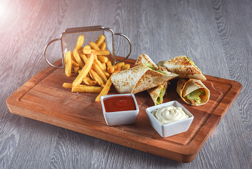 Burritos wraps with beef and vegetables on on a decorative board with tomato sauce and mayonnaise