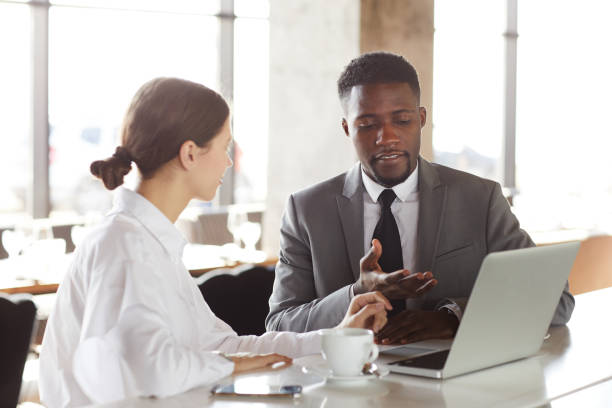 istock Content confident young black man in suit pointing at laptop monitor while presenting project to colleague at meeting in coffee shop 1146021520