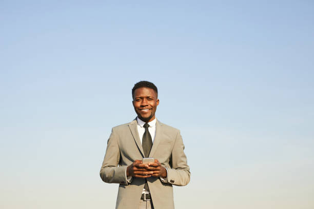 istock Smiling confident young African-American businessman with beard standing outside and using modern smartphone while checking messenger 1146022947