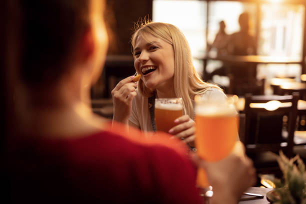 cheerful woman drinking beer and enjoying in conversation with female friend in a pub. - beer pub women pint glass imagens e fotografias de stock