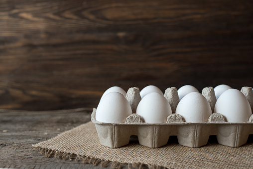 Raw white eggs in egg box on wooden background.