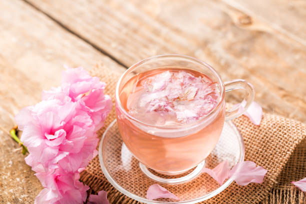 istock Spring tea. Cup of pink cherry blossom herb tea on wooden table 1146027425