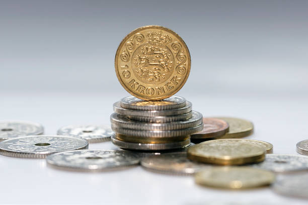 Ten Kroner coin standing on a stack of mixed Danish coins with selective focus. The krone is the official currency of Denmark, Greenland, and the Faroe Islands, introduced on 1 January 1875.