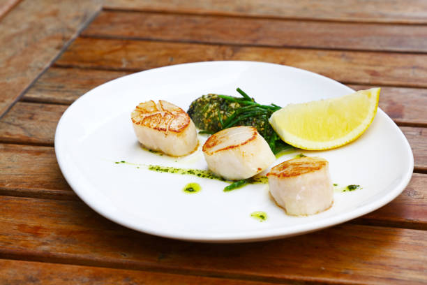 istock Portion of grilled scallops on plate on table 1146034824