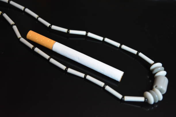 istock One cigarette and gray female beads on a black glossy background. 1146038033