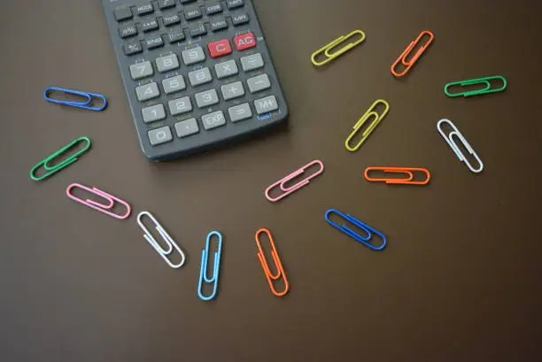 Photo of Color clips of different colors with a gray calculator on a brown matte background.