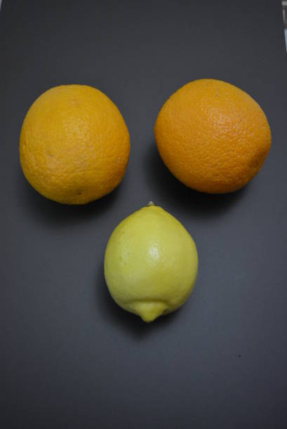 fresh fruits, two orange oranges with one yellow lemon on an interesting matte background. - lemon fruit portion citrus fruit imagens e fotografias de stock