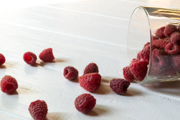 istock Ripe raspberry in a glass, on a white wooden table. 1146049028