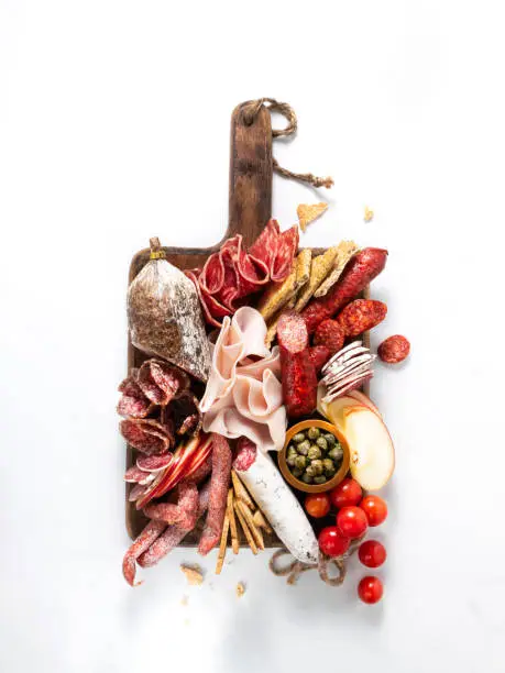 Cold meat plate, charcuterie on white background with copy space. Traditional Spanish tapas selection - chorizo, salchichon, jamon serrano, lomo, salami. Top view.
