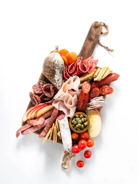 Cold meat plate, charcuterie on white background with copy space. Traditional Spanish tapas selection - chorizo, salchichon, jamon serrano, lomo, salami. Top view.