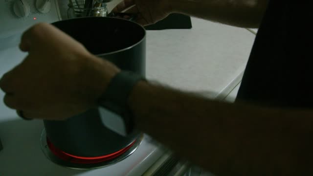A Caucasian Man Places a Large Pot on to a Stop Top Range Set to High Heat in a Kitchen