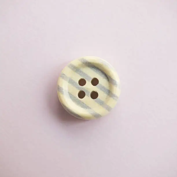 Photo of Isolated wooden button with colored colorful stripes on a light pink background, sewing