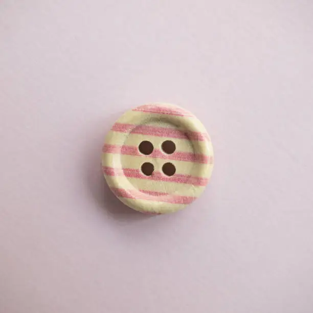 Photo of Isolated wooden button with colored colorful stripes on a light pink background, sewing