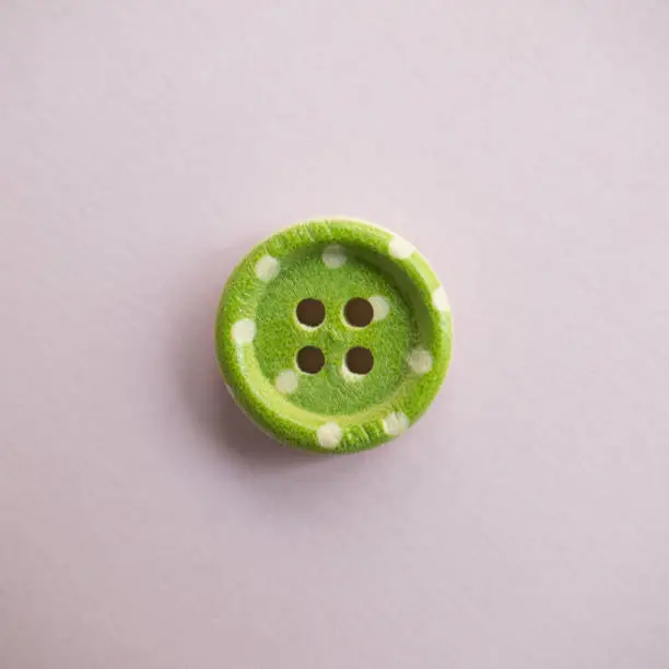 Photo of Isolated wooden button with colored colorful dots on a light pink background, sewing