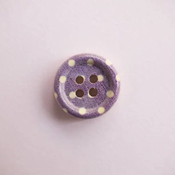 Photo of Isolated wooden button with colored colorful dots on a light pink background, sewing