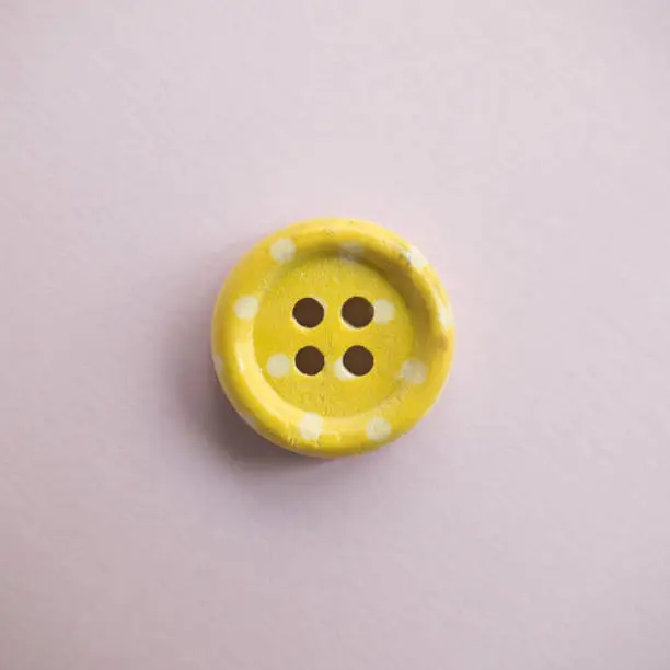 Photo of Isolated wooden button with colored colorful dots on a light pink background, sewing