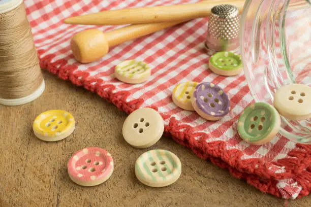 Photo of Wooden buttons with colored stripes of colors on a red and white checkered tablecloth, sewing