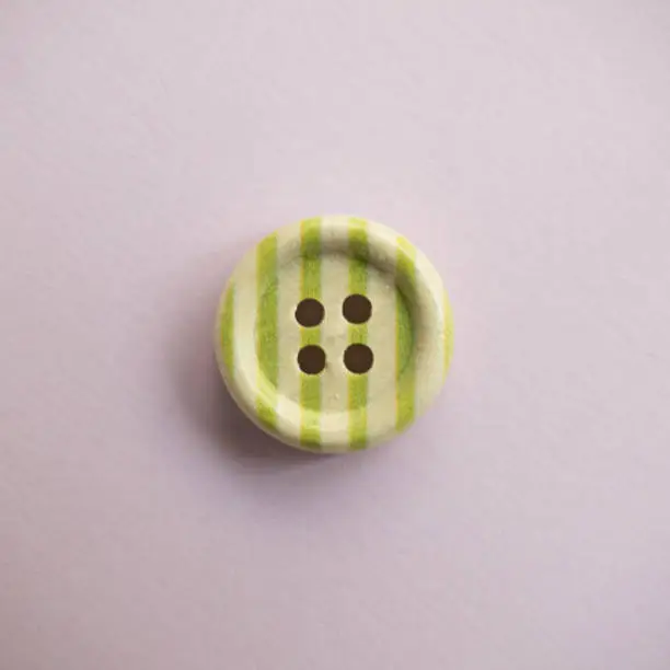 Photo of Isolated wooden button with colored colorful stripes on a light pink background, sewing