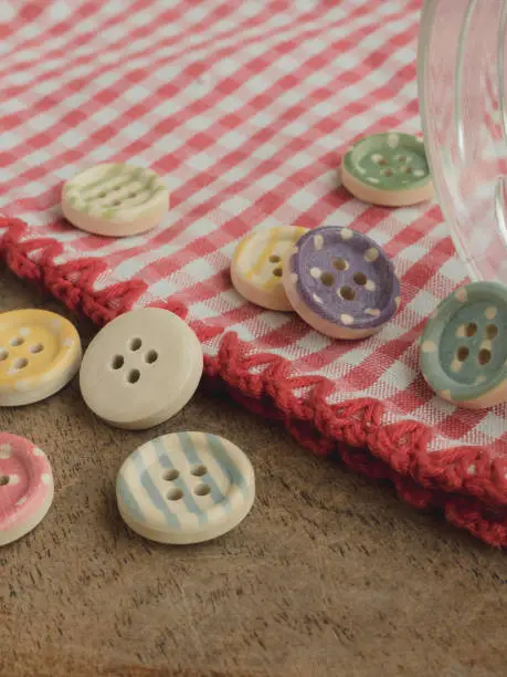 Photo of Wooden buttons with colored stripes of colors on a red and white checkered tablecloth, sewing