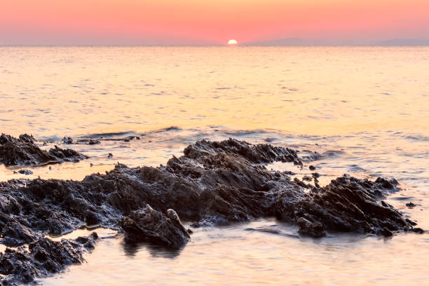 Setting Sun viewed from rocky reef on Paradisos beach in Neos marmaras Sharp layers of eroded rocks in the reflective sea water and the setting sun on the horizon on a reef near Paradaisos beach in Neos Marmaras halkidiki beach stock pictures, royalty-free photos & images