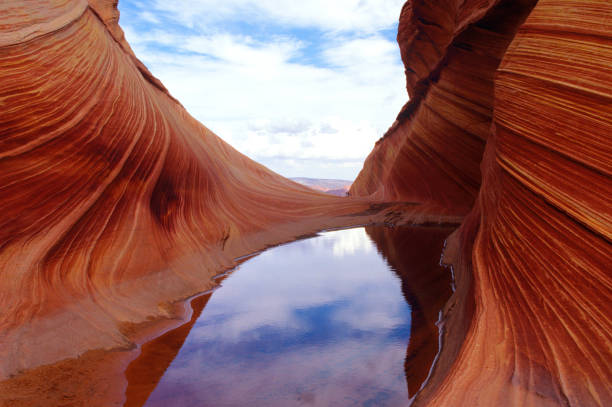 The Wave Looking North with Water Reflections in Coyote Buttes area of Vermilion Cliffs National Monument in Arizona Utah border area USA The Wave with water reflections is in the Coyote Buttes area of Vermilion Cliffs National Monument in Arizona USA.  After rain there are pools of water everywhere creating unusual abstract images.  Other worldly geology.  Surreal.  Sand dune layers turned to rock.  Arizona Utah border area.  High clouds passing bye. the wave arizona stock pictures, royalty-free photos & images